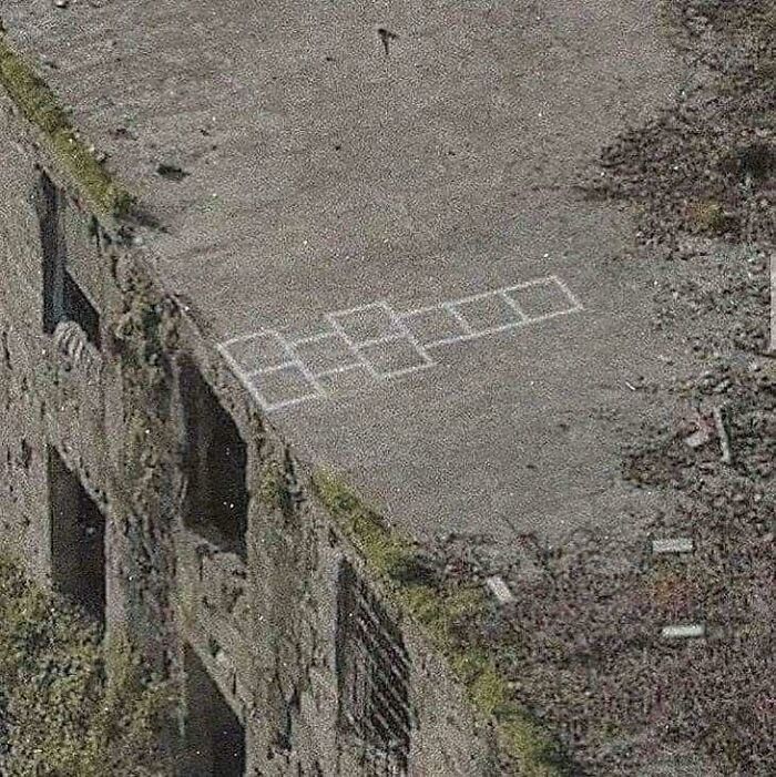 An aerial view of an old, weathered building with a hopscotch grid drawn on its roof, posing a baffling question.