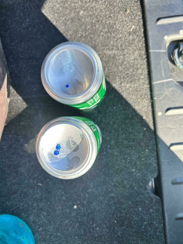Two aluminum cans with blue ink marks on their tops, placed on a dark surface, one of the baffling images.