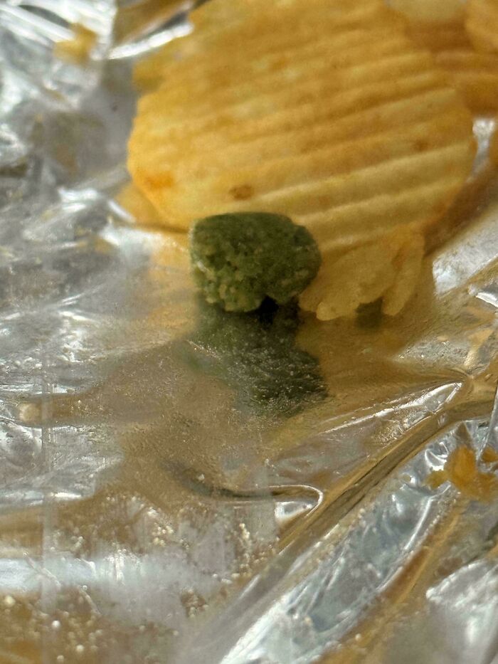 A baffling image showing a large green blob or piece of food in a potato chip bag with several ripple chips.
