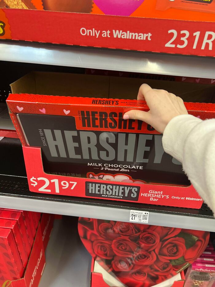 A baffling image of a hand reaching for a giant Hershey's milk chocolate bar, priced at $21.97, in a store aisle.