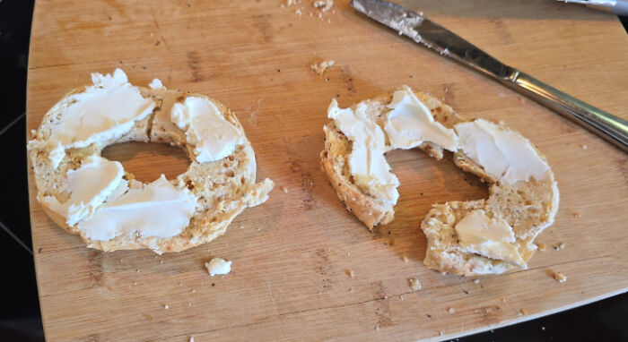Bagel halves spread unevenly with cream cheese on wooden cutting board