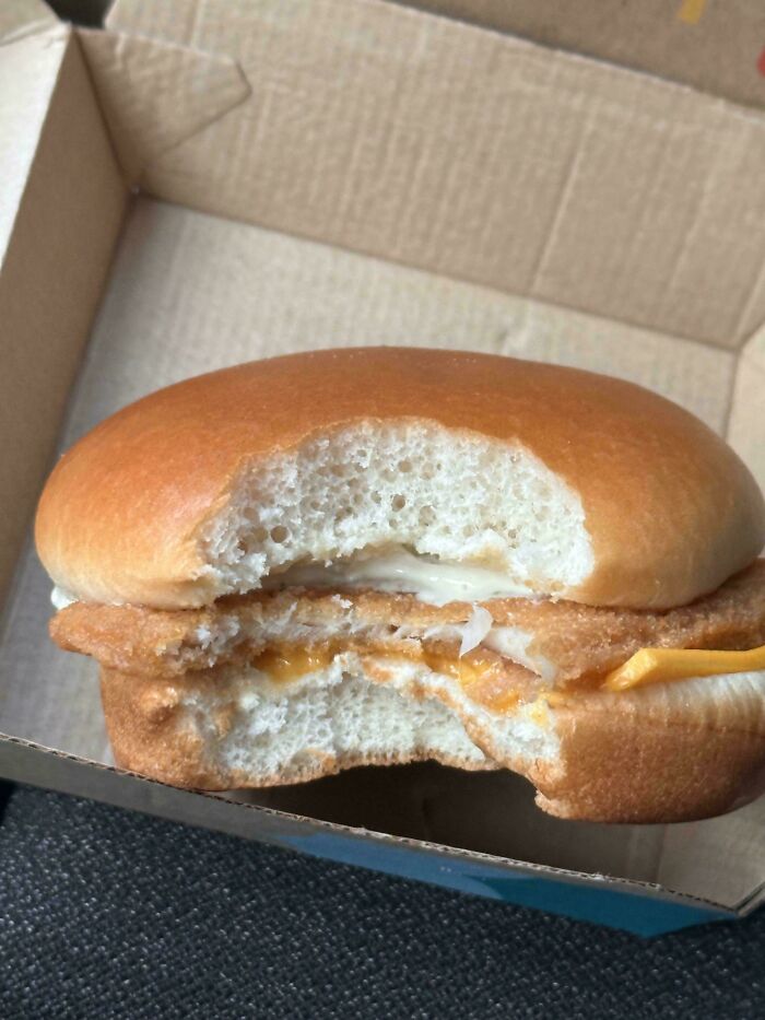 Fish sandwich with a bite taken exposing minimal cheese and fish inside bun scam