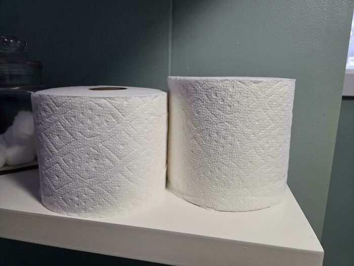 Two toilet paper rolls showing different sizes on a white shelf against a green wall