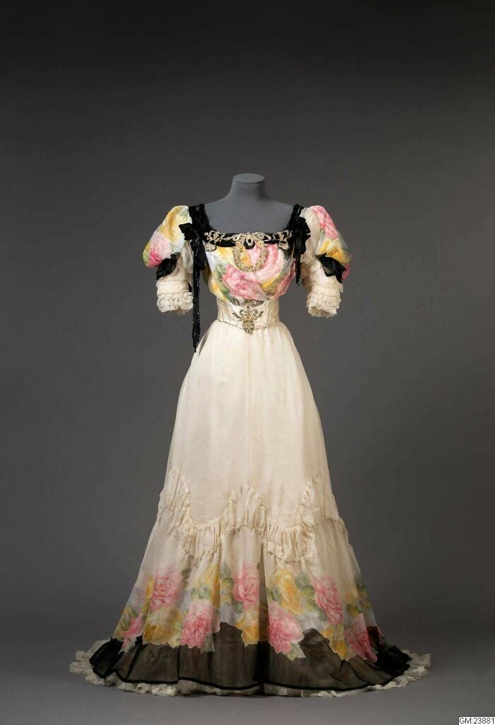 Ball Gown Made Of White Satin With Rose Pattern, The Neckline Is Edged With Black Velvet Ribbons And Ribbons Of Gold And Silver Thread With Floral Pattern, And Black Beads, The Center Front Has A Motif In Gold And Silver Thread, 1906. Gothenburg City Museum