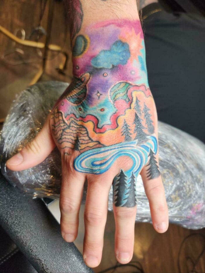 Colorful nature and space themed tattoo on hand with trees and rivers