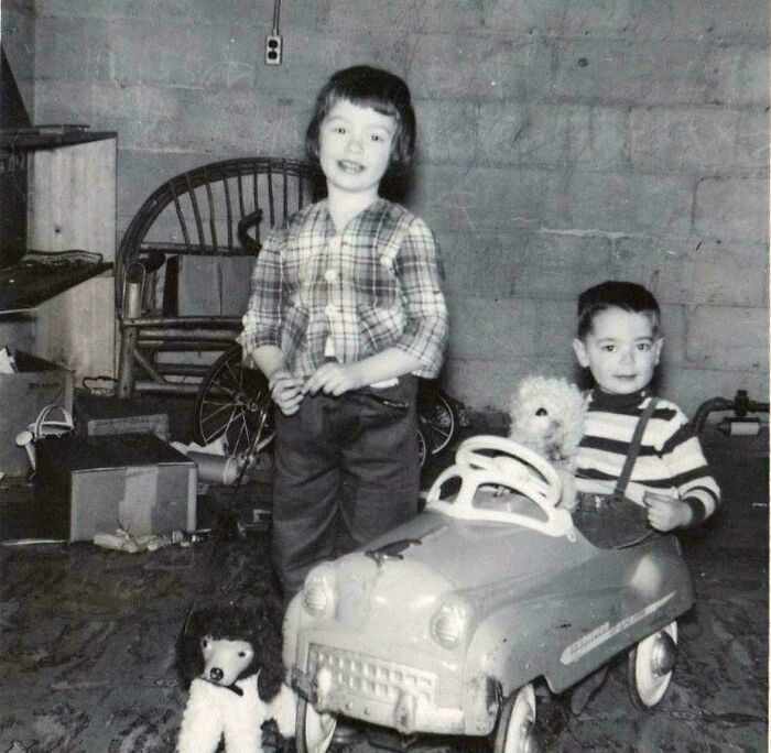 Two children play with a vintage toy car and stuffed dog in a basement, capturing decades-old photos with nostalgic charm.