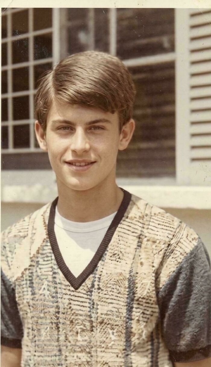 Young man from decades ago wearing vintage patterned sweater standing outdoors near a window, illustrating photos from decades ago.