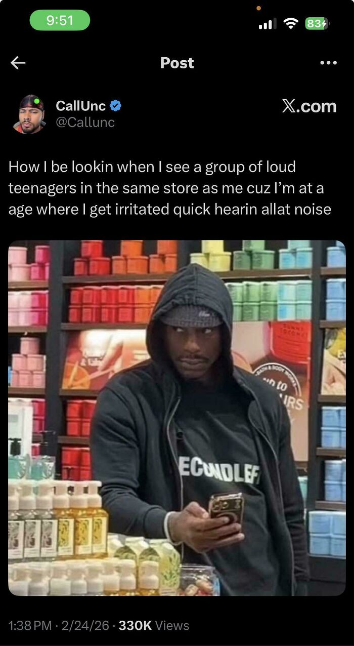 Black man in a hoodie, holding a phone, with a wary expression in a store. Important Tweets From Black Twitter.