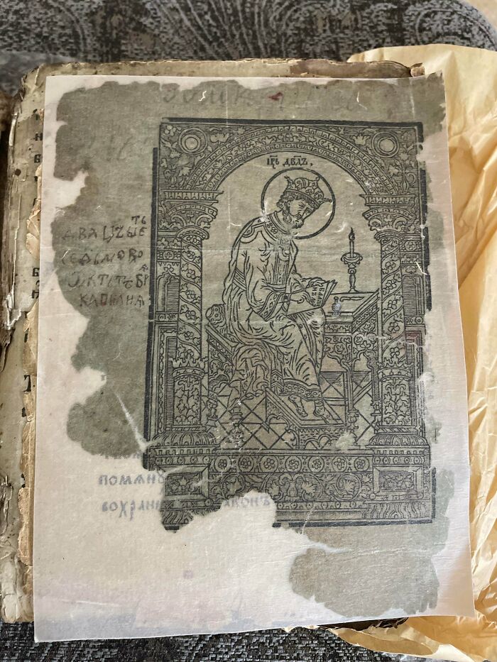 A remarkably detailed antique print depicting a regal figure reading, found within an old, delicate book.