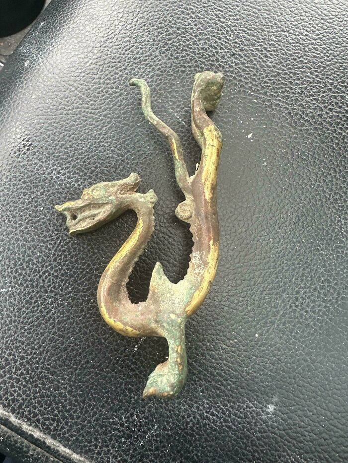 A remarkable antique dragon-shaped metal artifact, likely an old door handle or decorative piece, on a black textured surface.