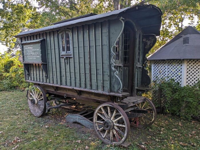 A vintage, remarkable antique green wooden wagon with weathered paint and large wooden wheels, parked on grass.