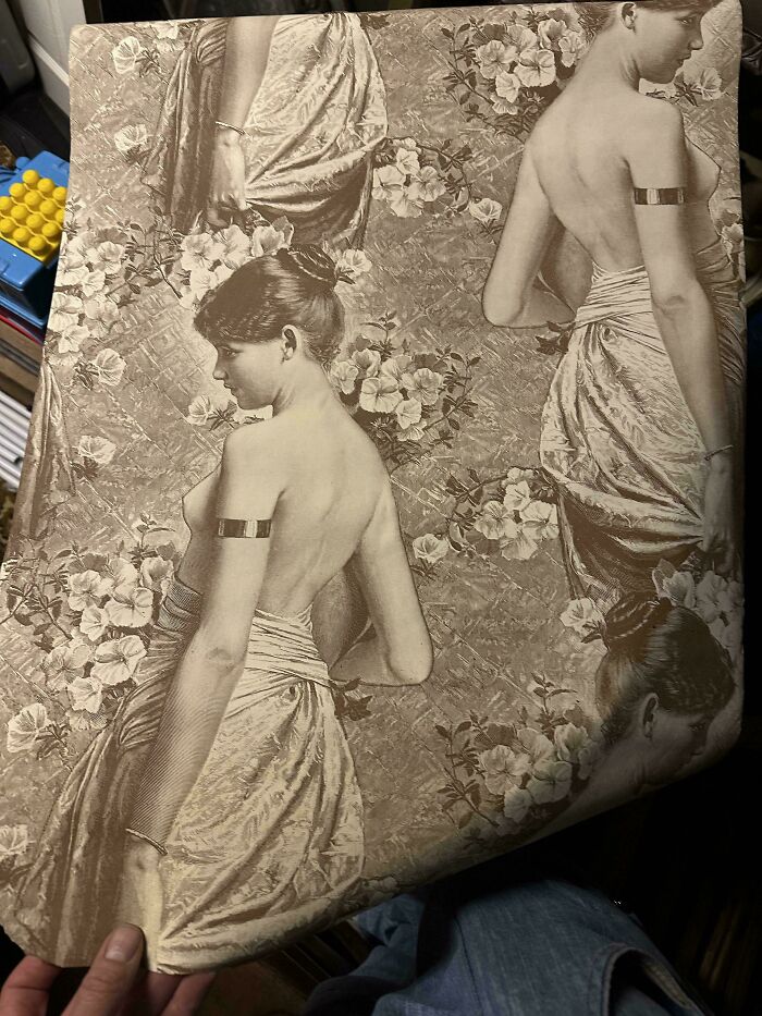 A piece of old wallpaper featuring remarkable antique illustrations of women draped in fabric, surrounded by flowers.