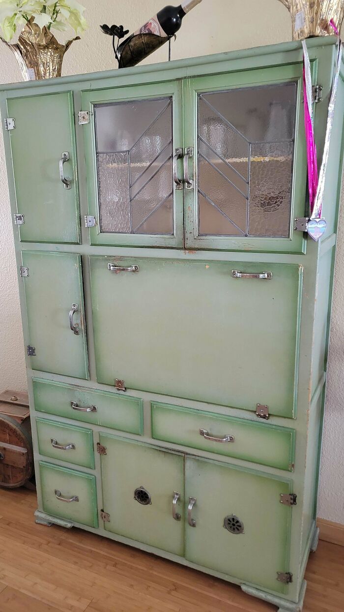 A tall, light-green cabinet with glass doors and multiple drawers, a remarkable antique piece of furniture.