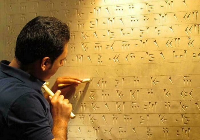 Man carving cuneiform script in clay wall archaeological discovery