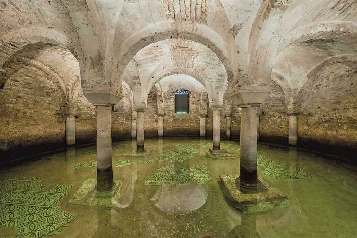 Historic underground chamber with stone pillars and mosaic floor partially submerged in water