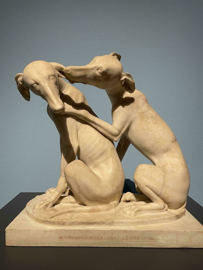 Marble sculpture of two greyhound dogs in an affectionate pose