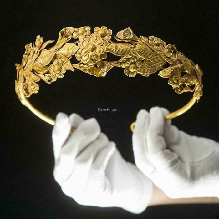 Ancient golden crown decorated with intricate floral designs held with white gloves