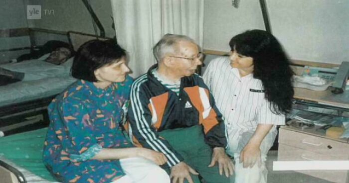 A historical photo shows two women sitting with an elderly man in a hospital room, a deeply emotional scene.