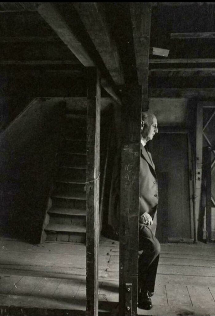 A historical photo captures a man standing in a dimly lit, dark room with wooden beams and stairs, a fascinating scene.