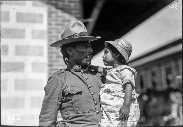 A man in a uniform and hat holds a young girl in this emotional historical photo.
