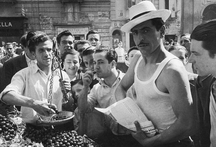 A fascinating historical photo of a crowd of men at a market, one weighing produce, another in a straw hat.