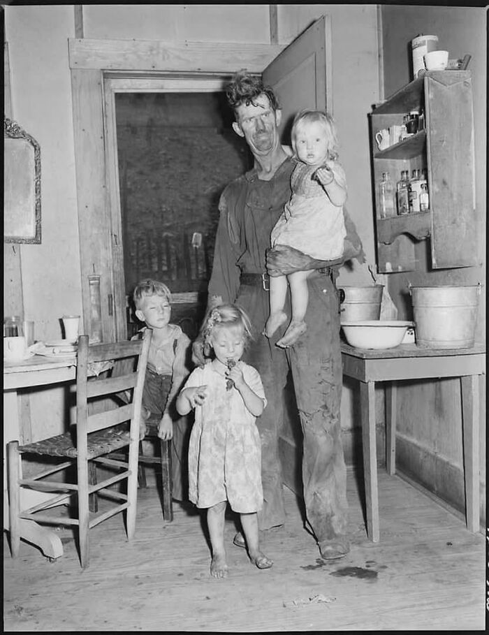 Fascinating historical photo of a man and three children in a simple room, showing an emotional moment from the past.
