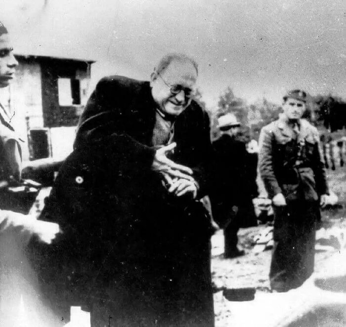 Emotional historical photo of a man in glasses gesturing with his hands, surrounded by others, evoking the past.