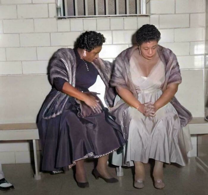 Two elegantly dressed women sitting on a bench, one comforting the other. A powerful historical photo.