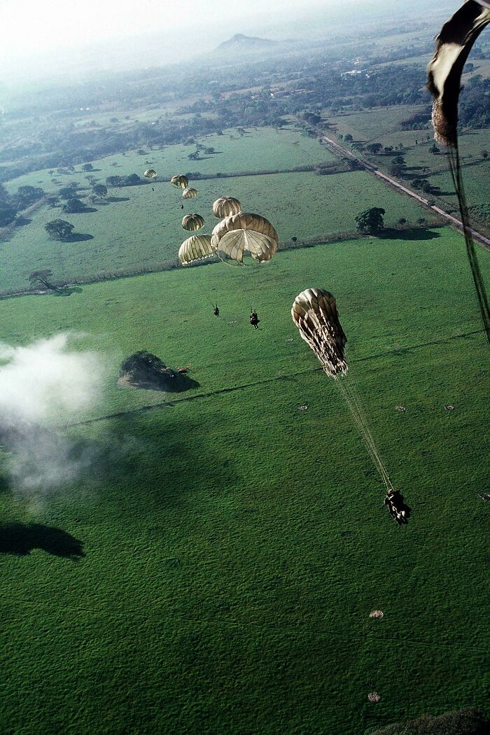 Paratroopers descend over a lush green field, a stunning sight among many emotional historical photos.