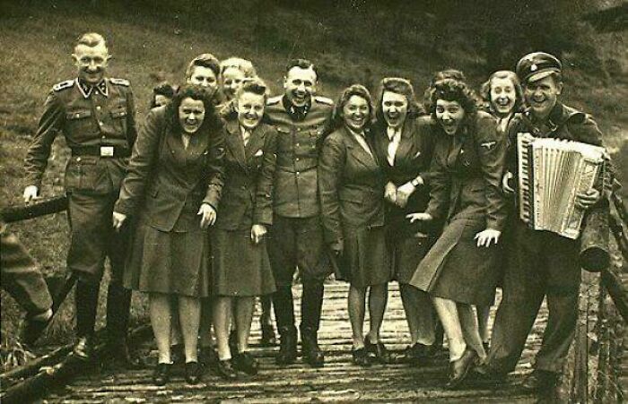 Fascinating historical photos of a group of soldiers and women smiling, with one soldier playing an accordion.