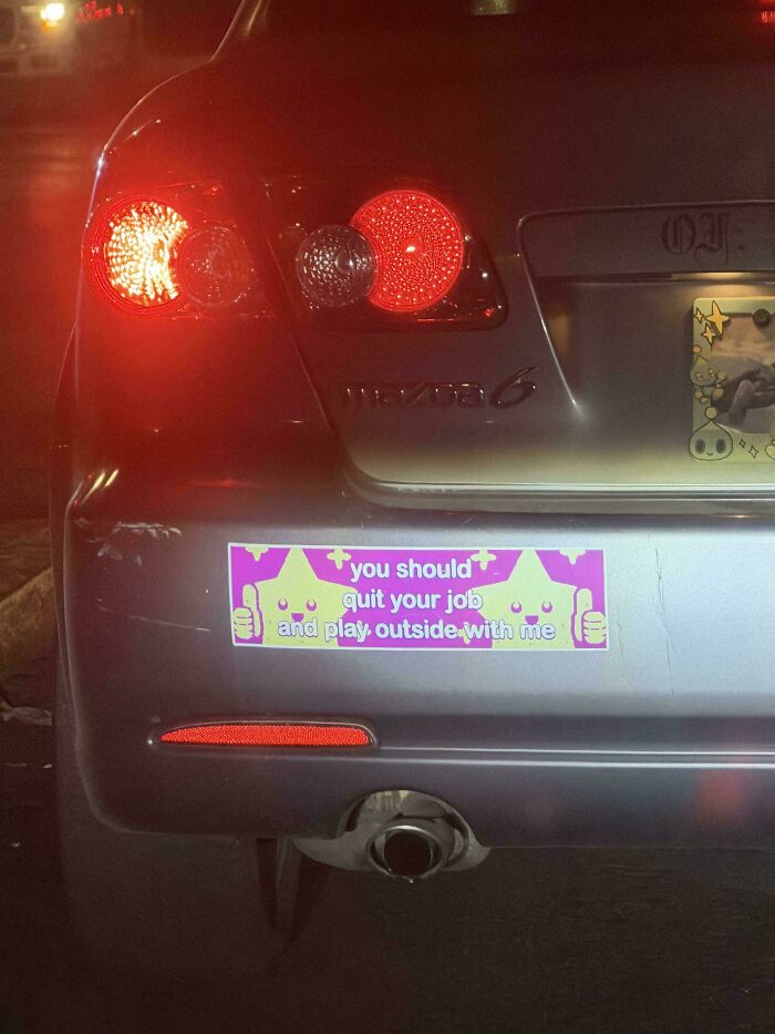 A rear view of a silver car with a funny bumper sticker that reads You should quit your job and play outside with me.