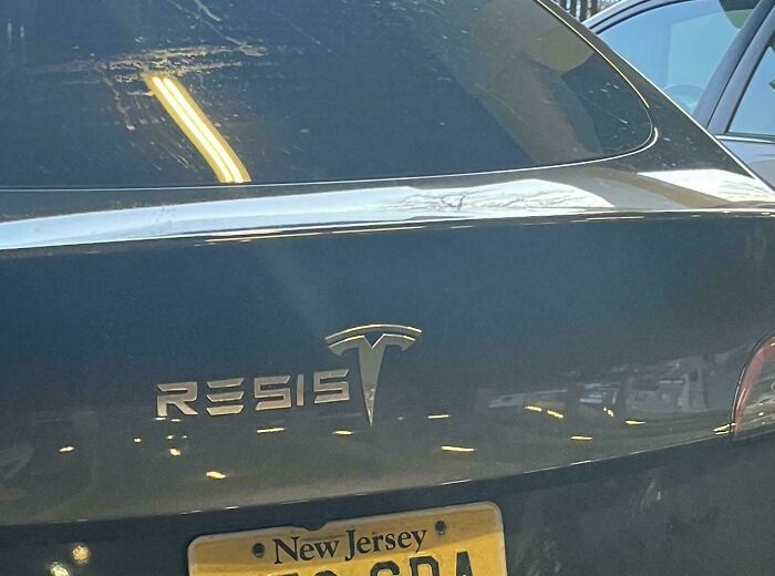 A funny bumper sticker on a Tesla that reads RESIST, with the Tesla logo replacing the T.