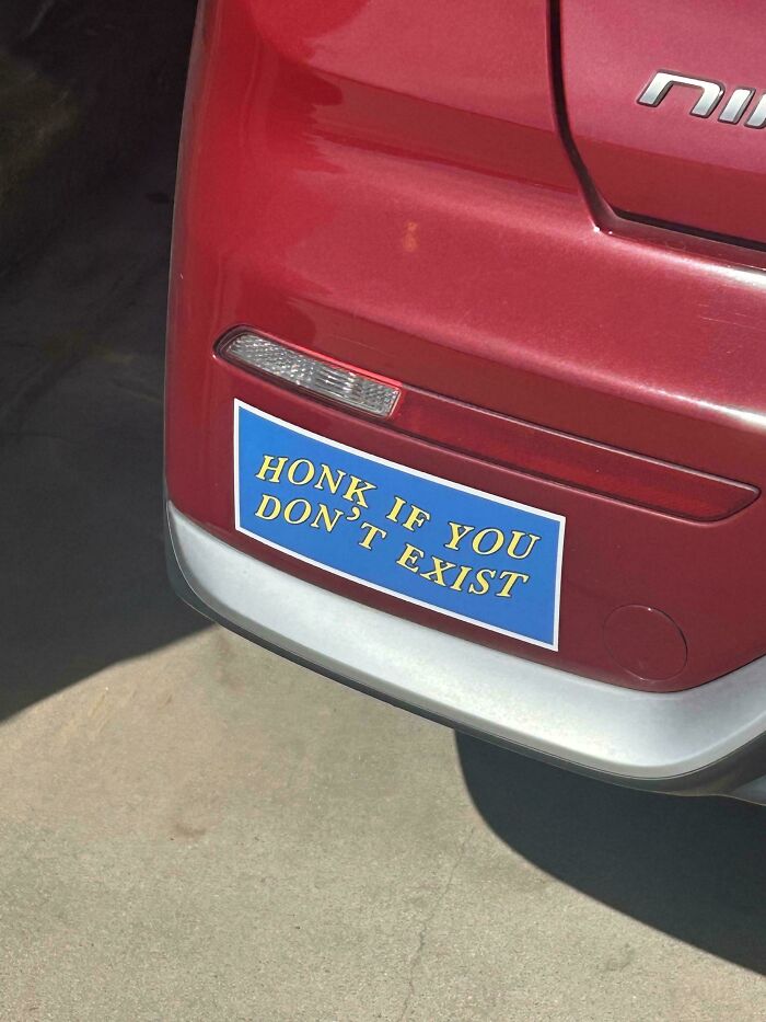 A funny bumper sticker on a red car reads Honk If You Don't Exist in yellow text on a blue background.
