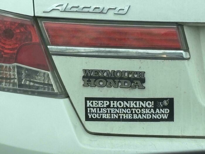 A funny bumper sticker on a white car reads Keep Honking! Im Listening To Ska And Youre In The Band Now.