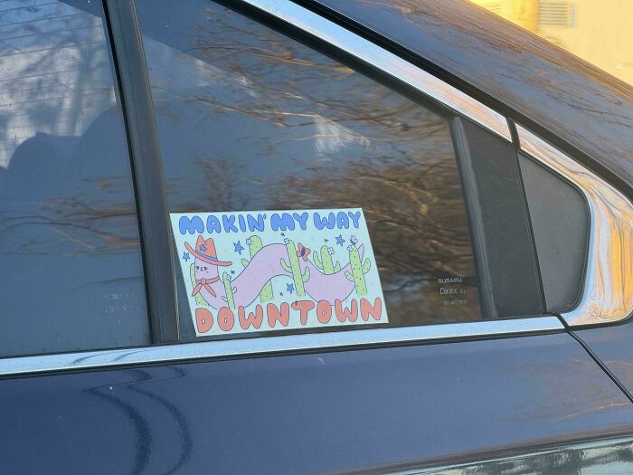 Wild bumper sticker on a car window depicting a cowboy riding a long pink worm with the text Makin' My Way Downtown.