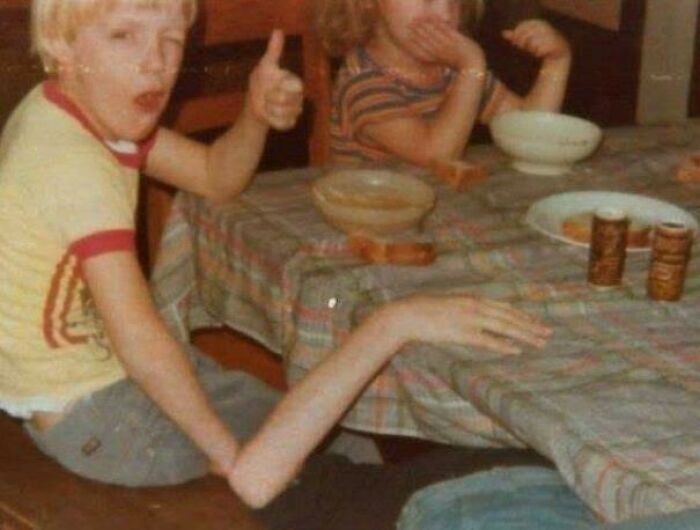 Child with an unusually long arm giving a thumbs-up at a table, an example of misleading and confusing photos.