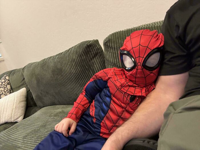 A child in a Spiderman costume sits on a couch next to an adult, a sweet moment for dads.