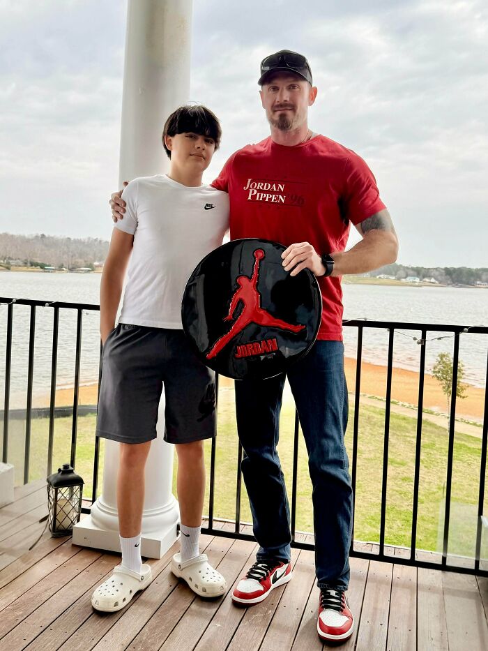 A dad and his son on a balcony with a lake view, the dad holding a Jordan logo, part of feel-good posts for dads.