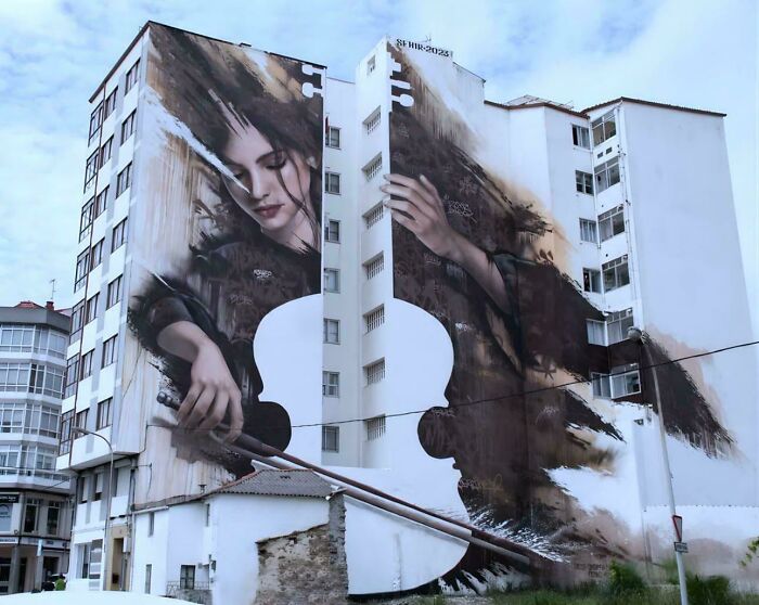 A giant mural of a woman holding a violin painted on the side of a tall building, an interesting photo.