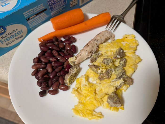 A frugal meal on a white plate: scrambled eggs with meat, kidney beans, and whole carrots, illustrating tips for this economy.