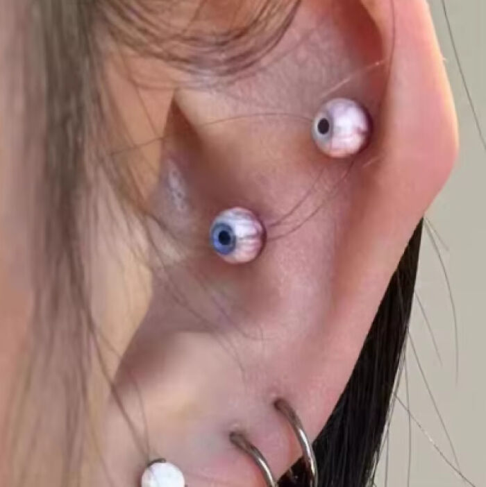 Close-up of ear piercings with eyeball-shaped jewelry