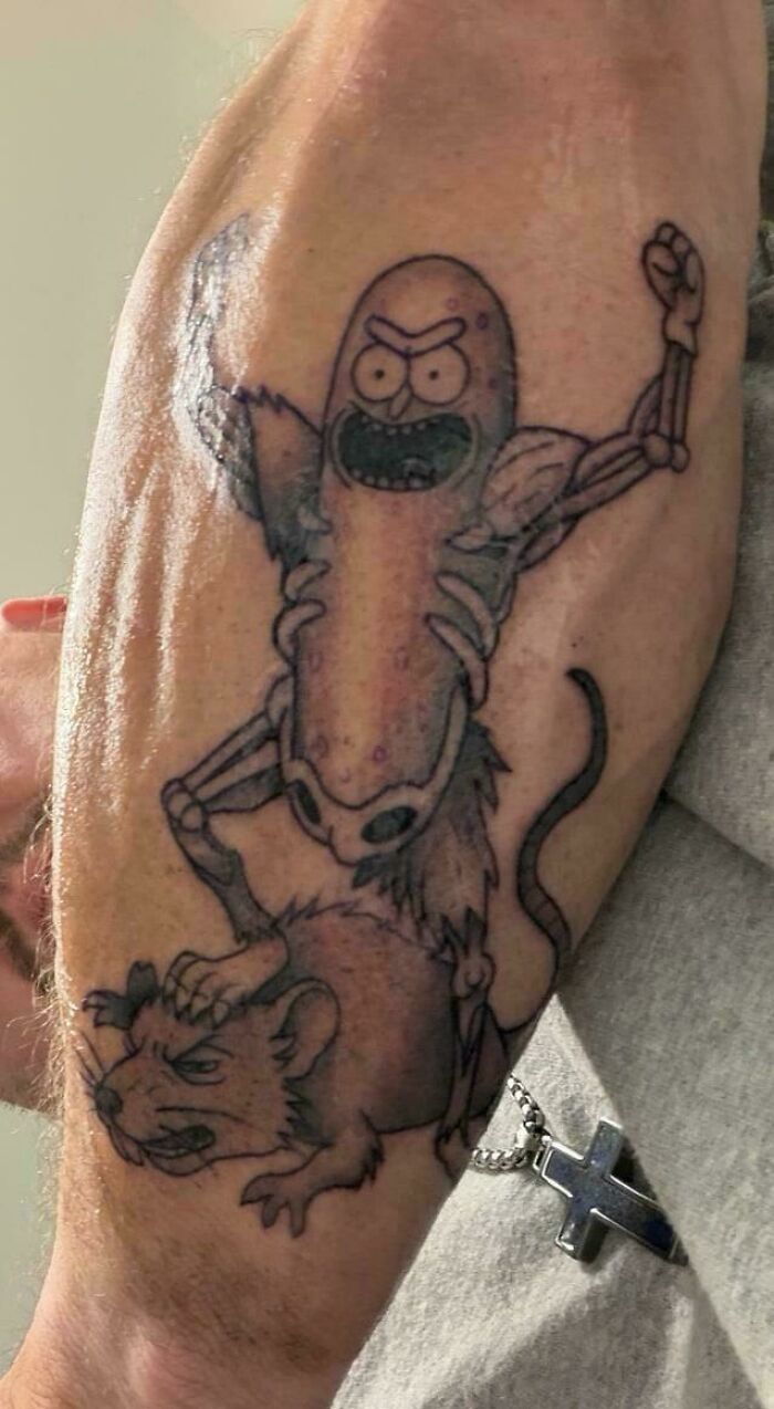 Tattoo of muscular cartoon pickle standing on angry rat on forearm