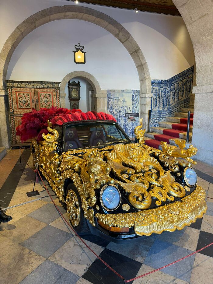 Car covered in ornate golden sculpture decorations in interior setting