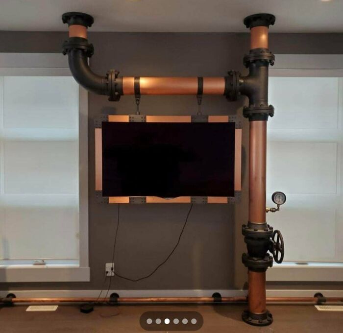 TV mounted on wall with industrial copper and black pipe frame