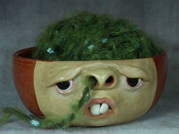 Humanoid ceramic bowl with green yarn hair and facial features including nose picking