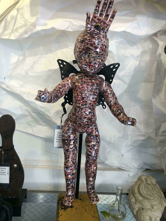 Figurine covered in multiple eye patterns with hand raised, displayed indoors