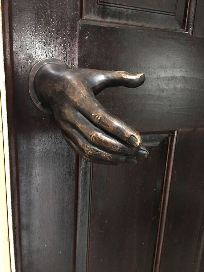 Unique door handle shaped like a realistic outstretched hand on a dark door