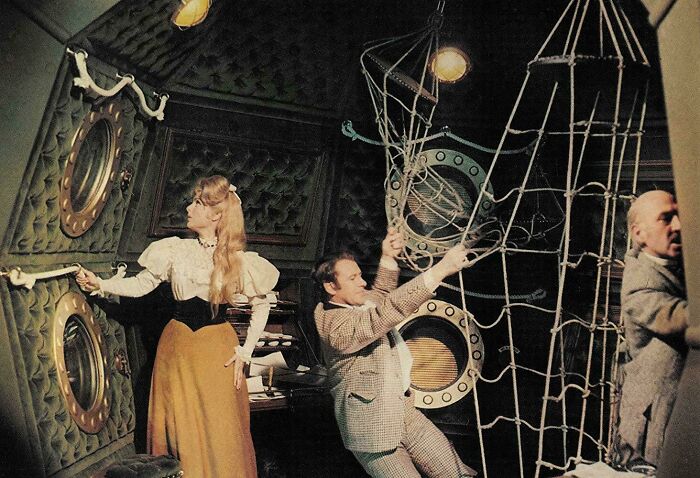 Retrofuturistic image: people in the past imagined the future with a woman and two men in a tilted, ornate room with a net.