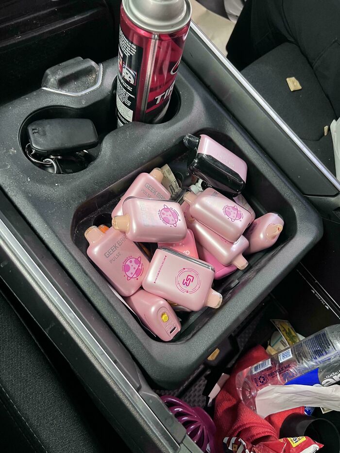A car console filled with numerous pink vape devices and car keys, an interesting discovery for car mechanics.
