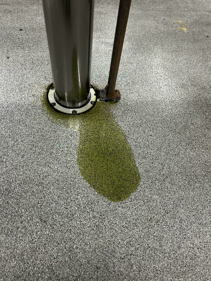 A vibrant green liquid stain on a gray speckled floor, depicting a messy car mechanics scenario.